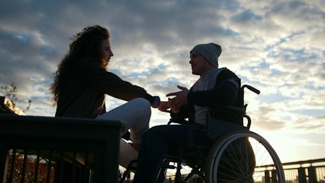 Man on a wheelchair talking to a young woman in the park.