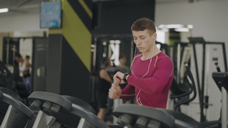 Man on treadmill in gym checks timer on watch