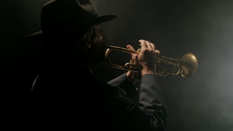 Man playing the trumpet in a smoky, dark room.