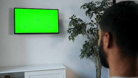 男子用遥控器指着墙上的绿屏电视
