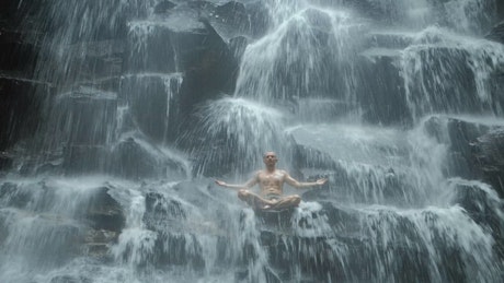 Man practicing mind body meditation in waterfall.