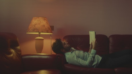 Man reads a book lying on the sofa in the lounge.