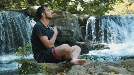 Man relaxing by a waterfall praying.
