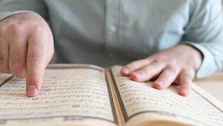 Man running his finger on the pages of the Quran