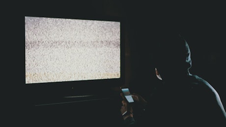 Man scrolling a phone in front of a television.