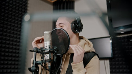 Man singing into a microphone in an audio booth.