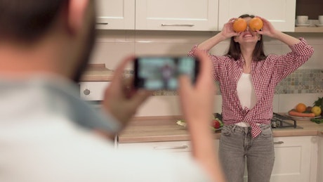 Man takes social media photo of woman on mobile in kitchen