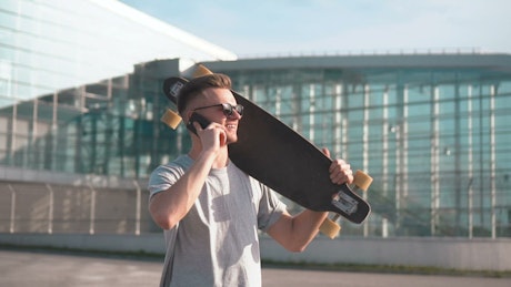 Man talking on the phone carrying a longboard.
