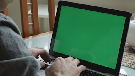 Man typing on a macbook with a green screen.