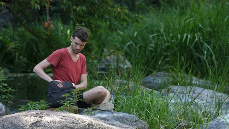 Man using a laptop by a stream.