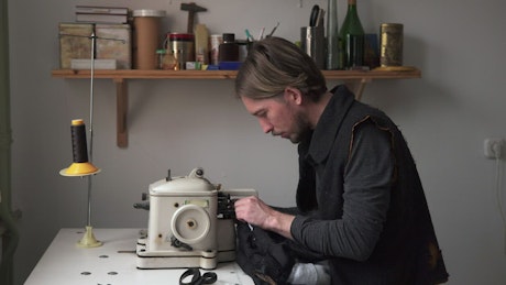 Man using a sewing machine to mend an item of clothes.