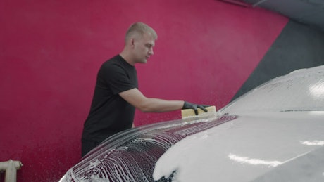 Man using a sponge to clean a soap-covered car.