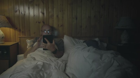 Man watching the tablet in the bedroom.