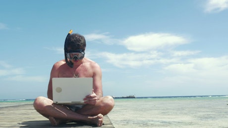 Man wearing a snorkel while using a laptop.