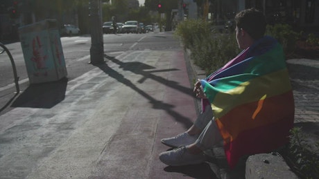 Man with a rainbow flag sits on the street