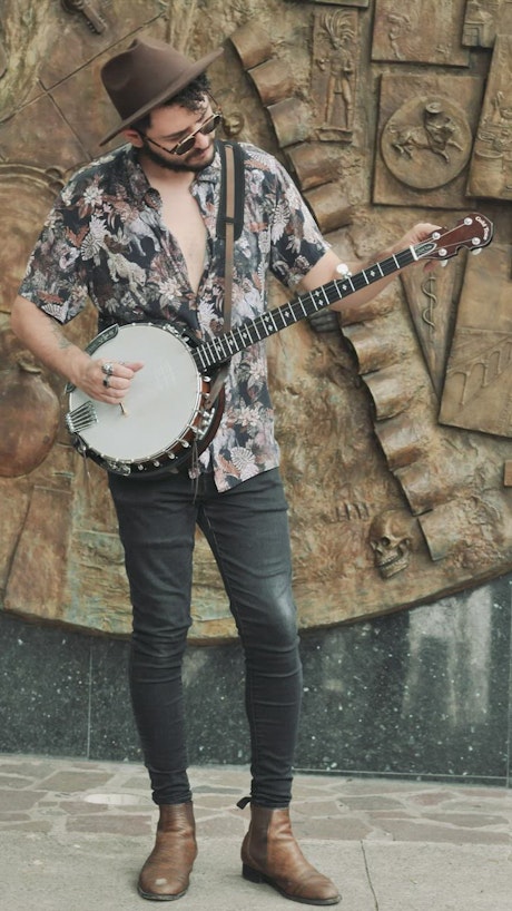 Man with dark glasses and hat while tuning his banjo