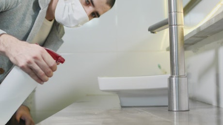 Man with face mask cleaning the surface of a bathroom