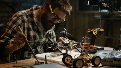 Man with glasses soldering a drone in the garage.