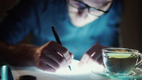 Man with insomnia writes with cup of tea