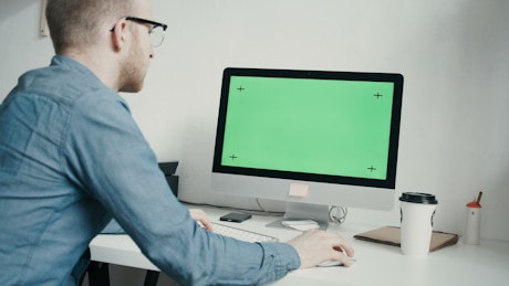 Man working on green screen monitor in minimal office.