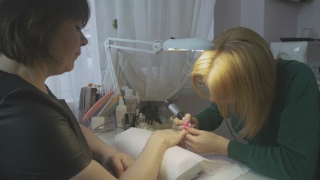 Manicurist clearing the nail surface.