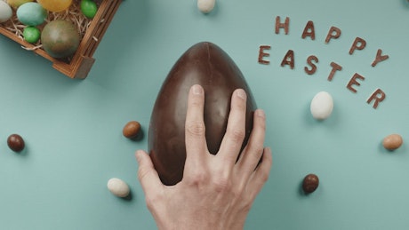 Man's hand opens a chocolate Easter Egg with a gift rabbit inside.
