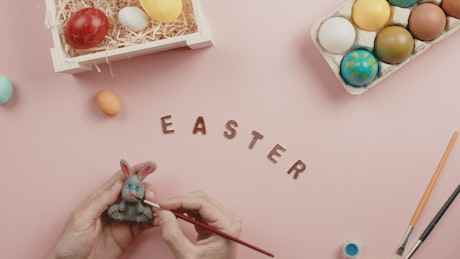 Man's hand Painting a Little Easter Rabbit with colorful Easter eggs.