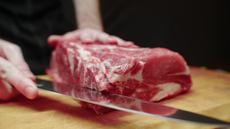Marbled piece of beef being expertly sliced by a chef.