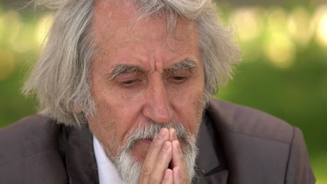 Mature man outside praying in a suit.