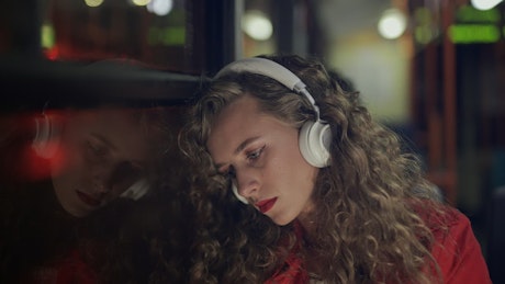 Melancholic woman with headphones on a bus at night.