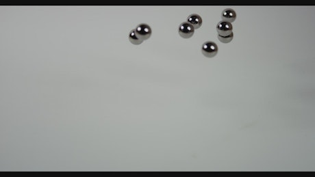 Metal pellets fall on white surface.