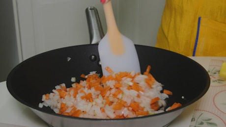 Mixing chopped vegetables in a frying pan.