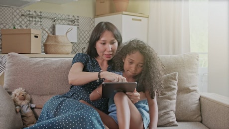Mother and daughter lounging on the couch looking at a tablet.