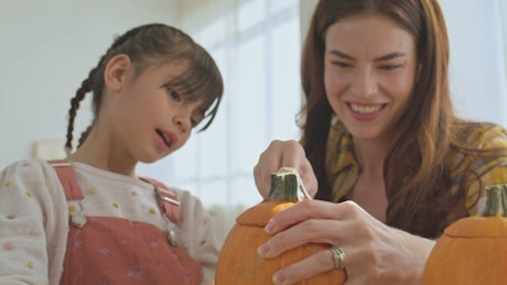 Mother and daughter making a pumpkin for halloween.