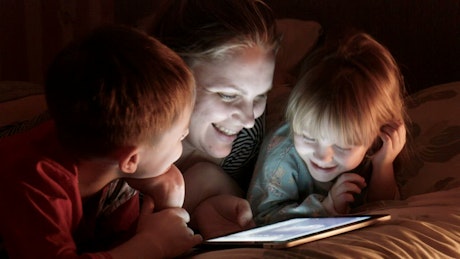 Mother and kids watching tablet on the bed.