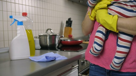 Mother cleaning a kitchen while she holds her baby.