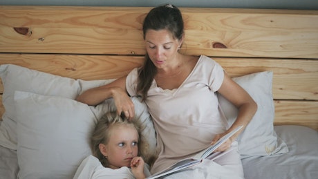 Mother reading her sleepy daughter a book before bed.