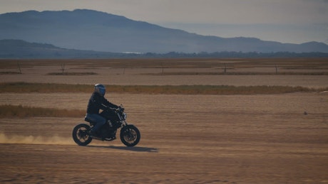 Motorcyclist crossing a desert surrounded by mountains.