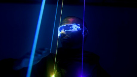 Neon laser lights dance off a man with cyberpunk glasses.