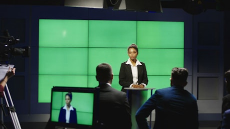 Newsroom presenter in front of green screen background.