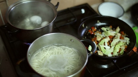 Noodles and vegetables cooking on a stove top.