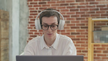 Office worker wearing headphones on a video call with a coworker.