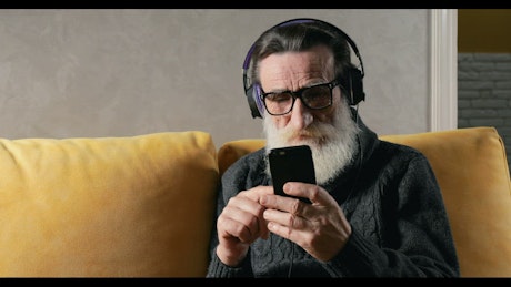 O|ld man listens to music with headphones on sofa.