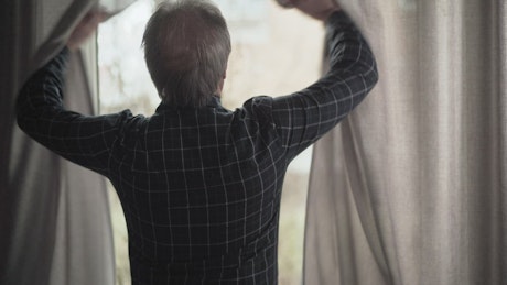 Old man opening the window curtains.