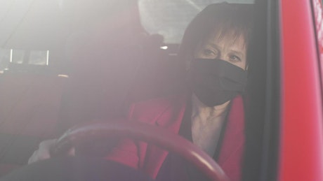 Old woman wearing mask while driving her car