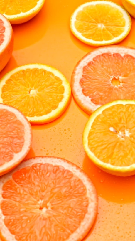 Orange and grapefruit fresh slices over a vibrant orange colored background.