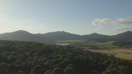 Panorama around a forest with a lake, a village and mountains.