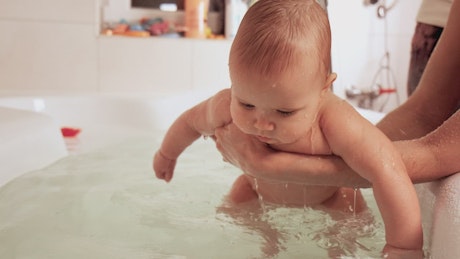 Parents bathing their baby in the tub.