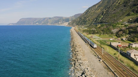 Passenger train traveling on seaside railway tracks.