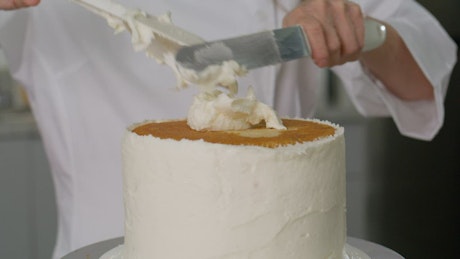 Pastry chef covering a cake with white icing.